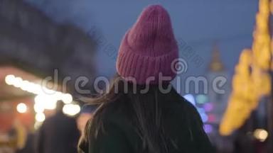 镜头跟随年轻的白种人妇女戴着粉红色的帽子和绿色的外套走到城市市场上的儿童旋转木马